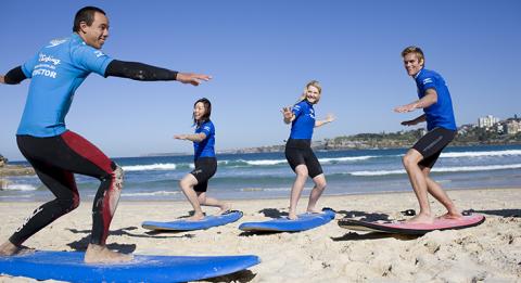 Zwei junge Frauen und ein junger Mann lernen bei einem „Let's Go Surfing“-Lehrer am Bondi Beach Surfen