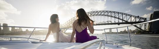 Zwei Frauen vor einer Yacht, die durch den Sydney Harbour segelt.